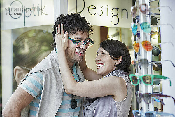 Glückliche Frau probiert ihrem Freund im Laden eine Brille an