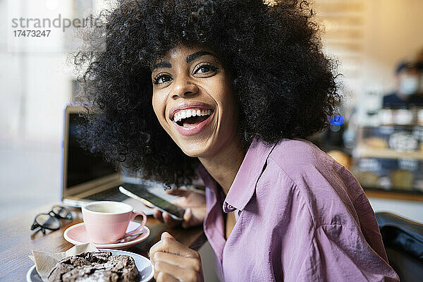 Lächelnde Frau mit Gebäck und Kaffeetasse am Cafétisch