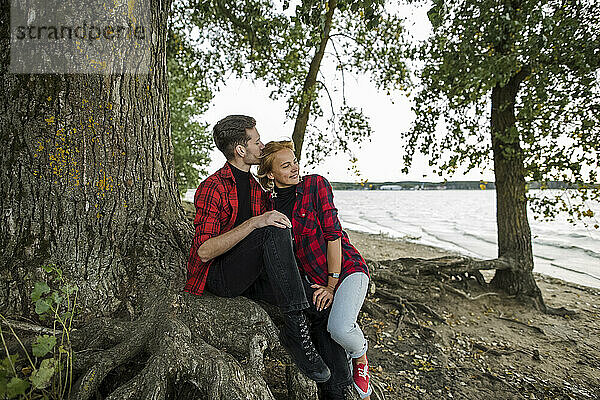 Mann küsst Frau  während er unter einem Baum sitzt