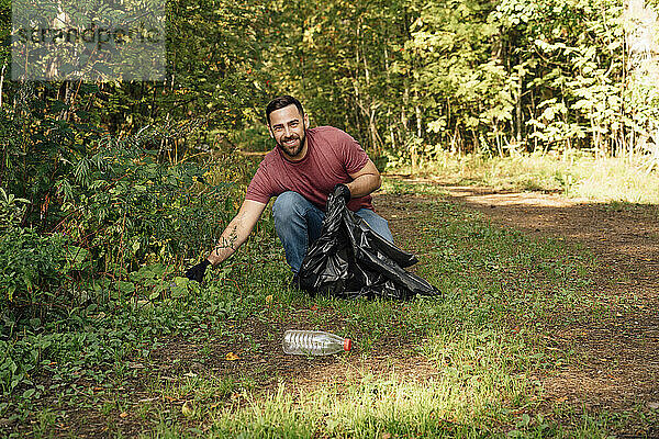 Lächelnder männlicher Umweltschützer sammelt Müll im Wald