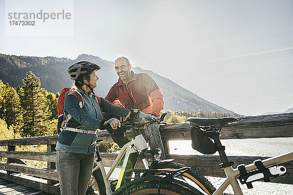Lächelnder Mann blickt Frau mit Fahrradhelm auf Brücke an