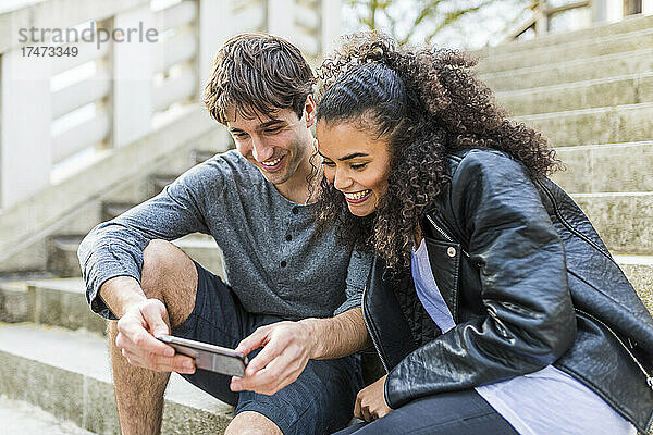 Mann und Frau teilen sich Smartphone und sitzen auf Stufen