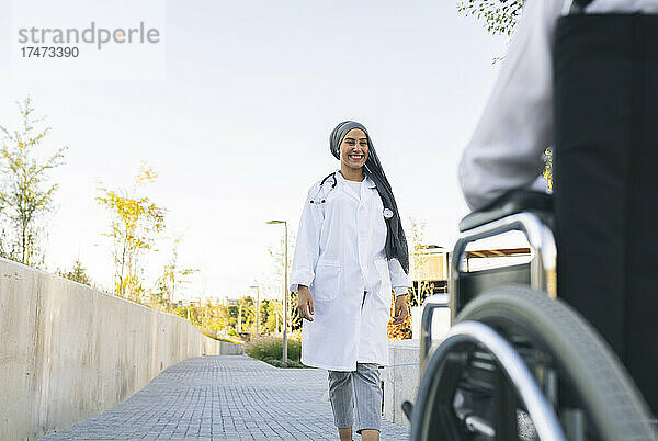 Lächelnde medizinische Fachkraft geht auf den im Rollstuhl sitzenden Patienten zu
