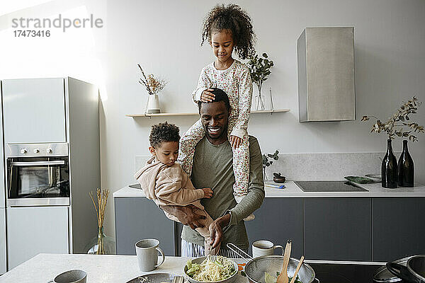 Lächelnder Vater trägt Tochter und Sohn in der Küche