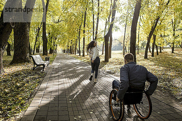 Freundin läuft mit behindertem Freund im Rollstuhl im Park