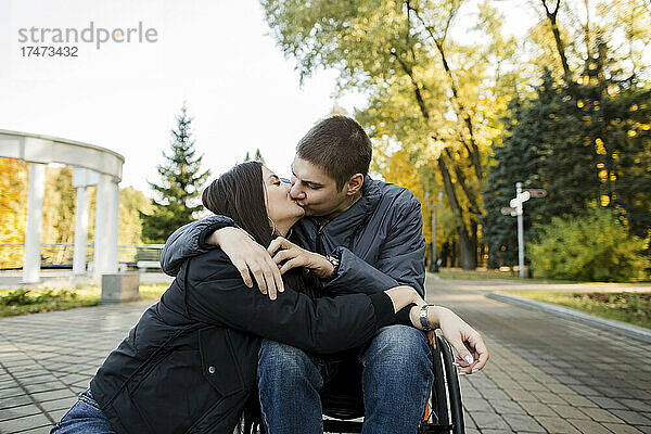 Freund im Rollstuhl küsst Freundin im Park