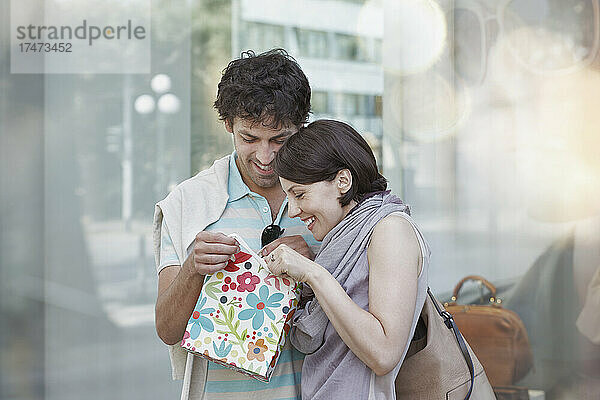 Lächelndes Paar schaut beim Einkaufen in die Geschenktüte