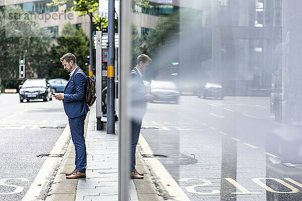 Geschäftsmann mit Rucksack benutzt Mobiltelefon auf Fußweg