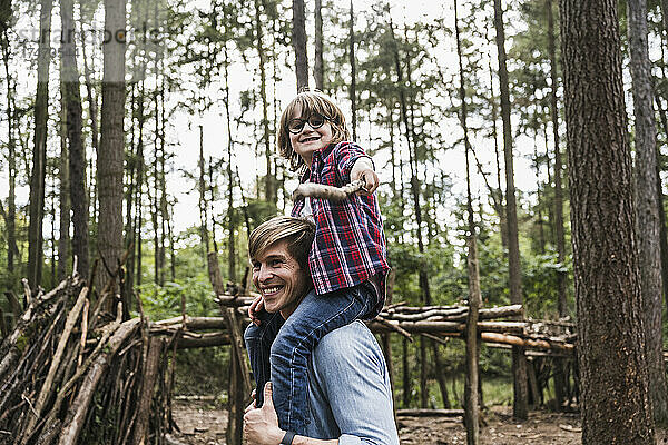 Lächelnder Mann trägt Jungen auf Schultern im Wald