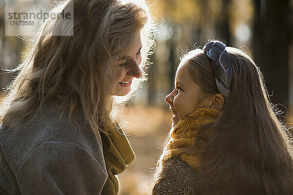 Lächelnde Mutter und Tochter sitzen sich im Herbstpark gegenüber