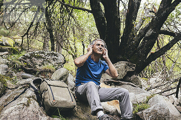 Lächelnder männlicher Tourist  der im Wald Musik über drahtlose Kopfhörer hört