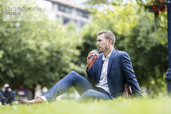 Geschäftsmann trinkt etwas  während er im Park sitzt