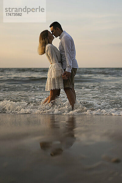Junges Paar reibt sich die Nase  während es am Strand im Meer steht
