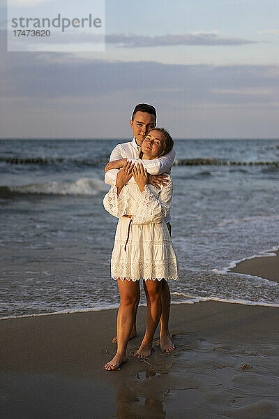 Junger Freund umarmt Freundin vor dem Meer am Strand