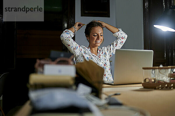 Junge Geschäftsfrau bindet Haare  während sie am Schreibtisch im Büro sitzt