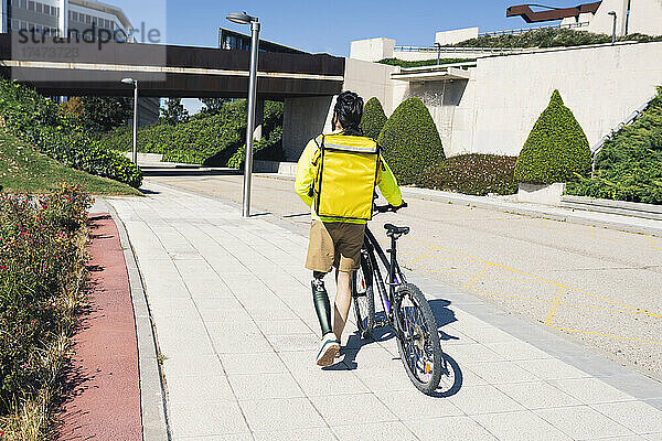 Lieferbote mit Beinprothese rollt Fahrrad auf Fußweg
