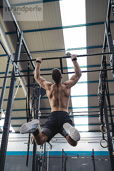 Nackter Oberkörper männlicher Athlet  der beim Training im Fitnessstudio am Klettergerüst hängt