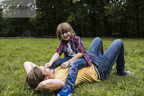 Junge spielt mit Vater  der im Park auf Gras liegt