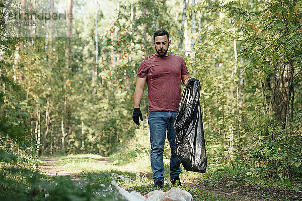 Männlicher Klimaaktivist mit Müllsack spaziert im Wald