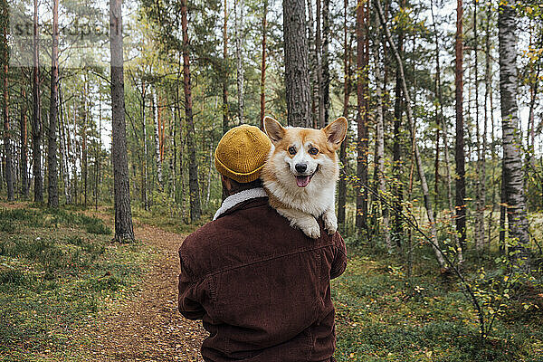 Mann trägt Hund auf Fußweg im Wald