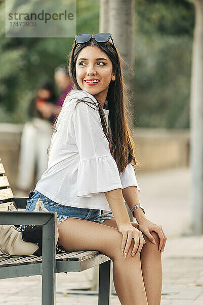 Junge Frau mit den Händen auf dem Knie sitzt auf einer Bank