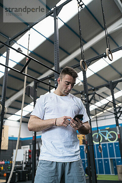 Junger männlicher Athlet benutzt Mobiltelefon im Fitnessstudio