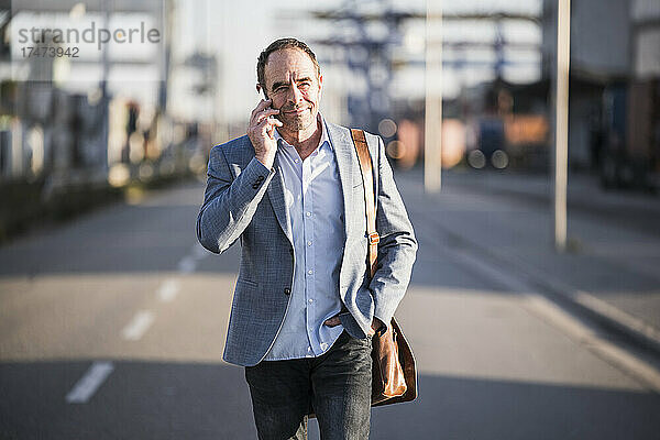 Reifer Geschäftsmann spricht mit Smartphone  während er auf der Straße geht