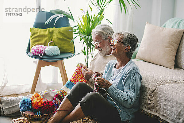 Lächelndes älteres Paar  das zu Hause gemeinsam Wolle strickt