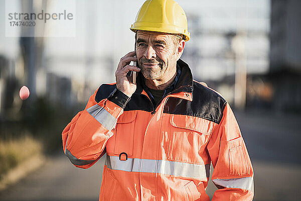 Reifer männlicher Arbeiter  der in der Industrie über Mobiltelefon telefoniert