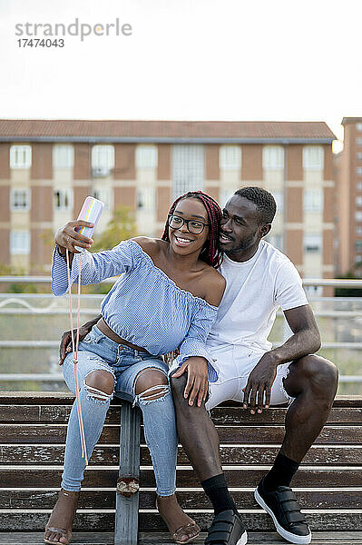 Lächelndes junges Paar macht Selfie auf Bank