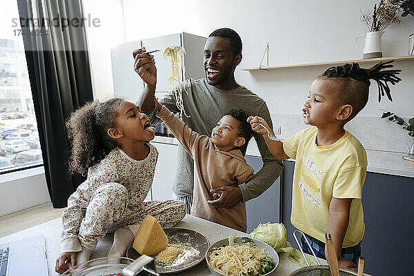 Glücklicher Mann füttert seine Tochter in der Küche mit Spaghetti