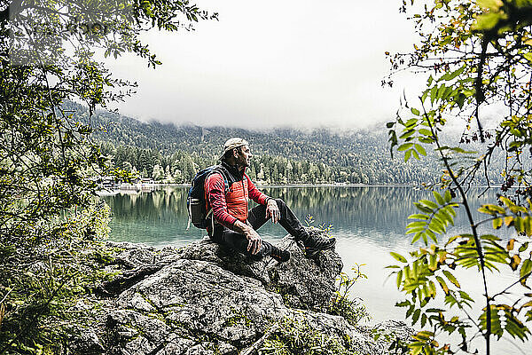 Männlicher Wanderer mit Rucksack sitzt auf einem Felsen im Wald