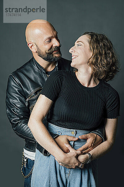 Lächelndes Paar umarmt sich vor grauem Hintergrund