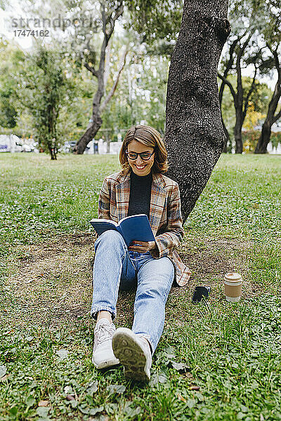 Lächelnder Freiberufler liest Buch vor Baum im Park