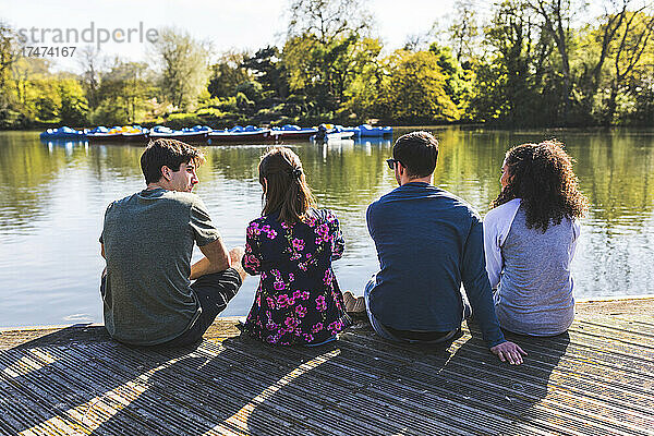 Freunde sitzen nebeneinander am Teich im Park