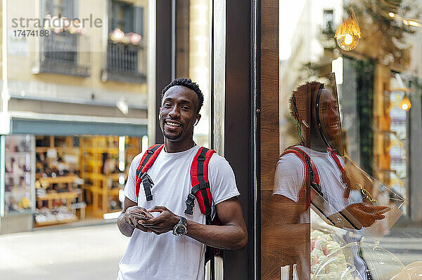 Lächelnder Tourist mit Rucksack  der an einer Glaswand lehnt