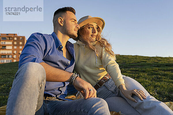 Junges Paar sitzt bei Sonnenuntergang zusammen auf einem Hügel