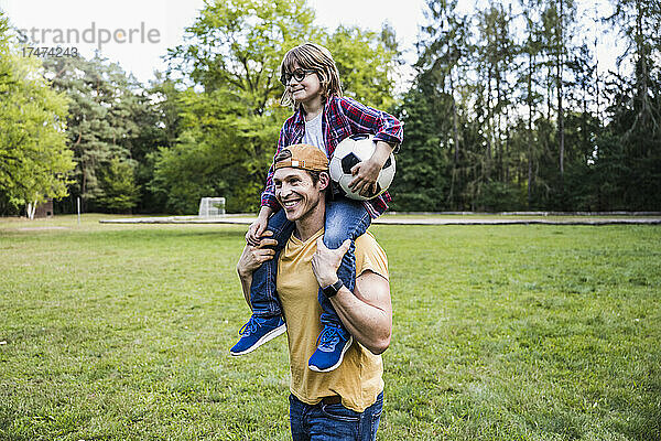 Lächelnder Vater trägt Sohn auf Schultern im Park