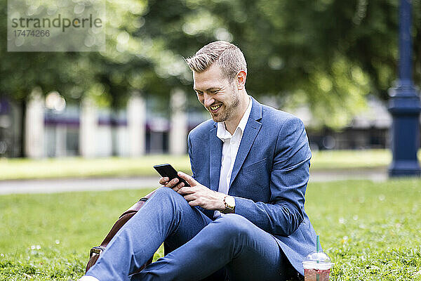 Lächelnder männlicher Profi  der im Park sein Mobiltelefon benutzt