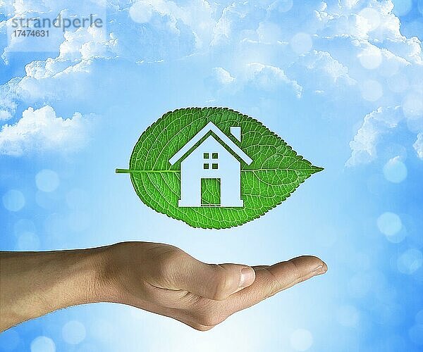 Geöffnete Hand hält ein grünes Blatt mit einem Haus-Symbol im Inneren auf einem blauen Himmel Hintergrund. Öko-Haus-Konzept