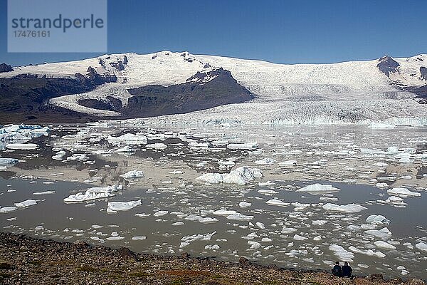 Menschen sitzen sitzen an einem See  Eisberge und Gletscher spiegeln sich in einem See  Gletscher und Berge im Hintergrund  Fjallsarlon  Vatnajökull Nationalpark  Island  Europa