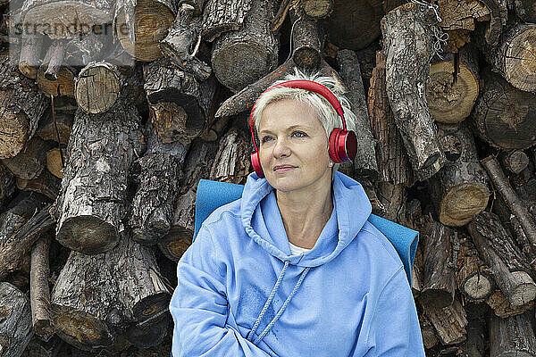 Gelassene Frau  die mit Kopfhörern am Holzstapel Musik hört