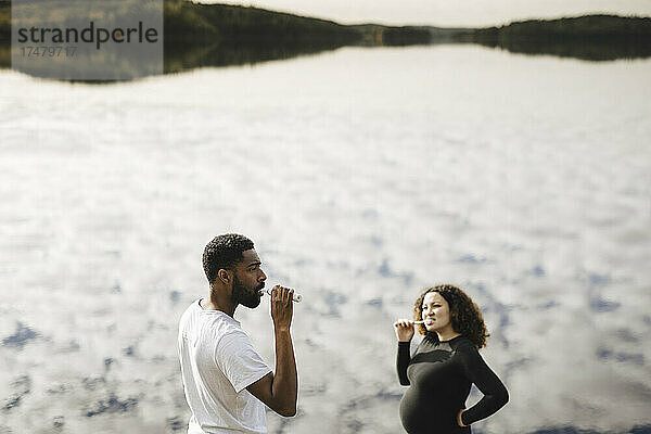 Junge schwangere Frau beim Zähneputzen mit ihrem Freund am Morgen am See
