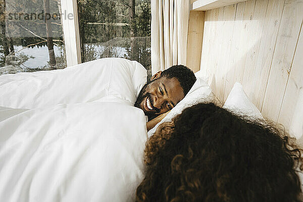 Glücklicher Mann schaut seine Freundin an  während er auf dem Bett im Hotel liegt