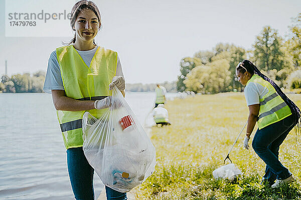 Porträt einer lächelnden Frau mit Plastiktüte am Seeufer