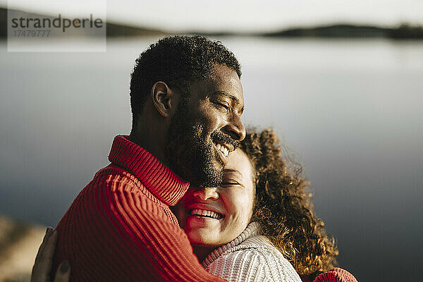 Glückliches Paar umarmt sich am See an einem sonnigen Tag
