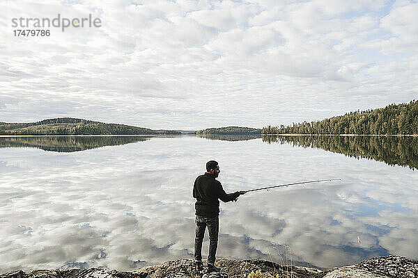 Rückansicht eines Mannes beim Fischen im See mit Wolkenreflexion in voller Länge