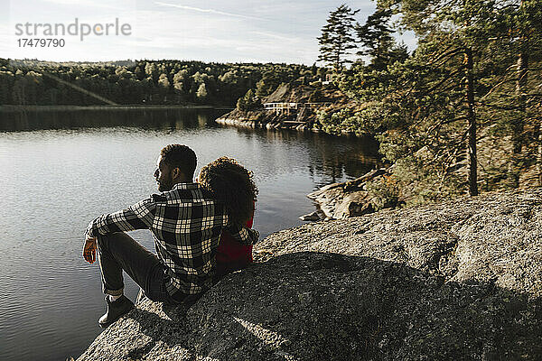 Heterosexuelles Paar verbringt seine Freizeit auf einem Felsen am See sitzend