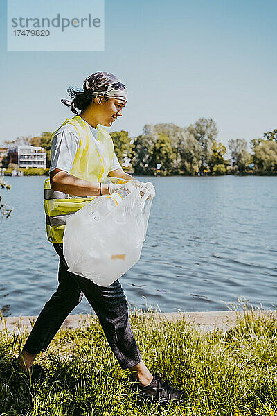 Umweltschützerin beim Spaziergang mit Plastiktüte am See