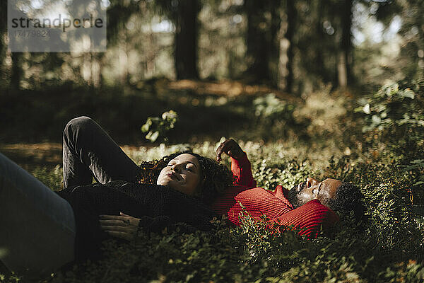 Schwangere Frau entspannt sich  während sie mit ihrem Freund auf Pflanzen im Wald liegt